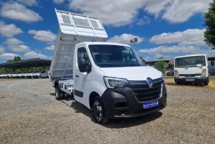 Renault Master Benne blanc en 3/4 avant droit, benne relevée et roues jumelées visibles sur terrain gravillonné.