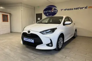 Vue 3/4 avant droite d'une Mazda2 blanche 2023 en hybride essence, avec calandre noire et plaque "OCCASION" en intérieur showroom.