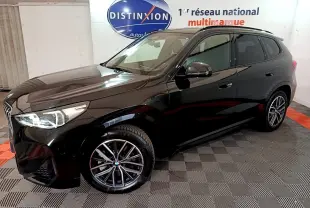 BMW X1 xDrive23i M Sport noir en 3/4 avant droit, avec jantes alliage et phares LED visibles en intérieur showroom