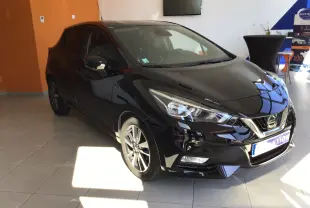 Nissan Micra noire vue en 3/4 avant droit dans un showroom, avec jantes alliage et calandre chromée.