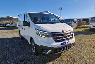 Renault Trafic Fourgon blanc vu en 3/4 avant droit, avec calandre noire et phares LED allumés, sur parking extérieur.
