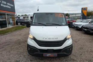 Vue de face d'un utilitaire Iveco Daily blanc avec calandre noire et phares allumés sur un parking.