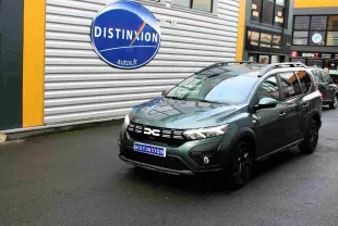 Dacia Jogger vert cèdre métal en 3/4 avant droit, avec calandre noire et barres de toit visibles.