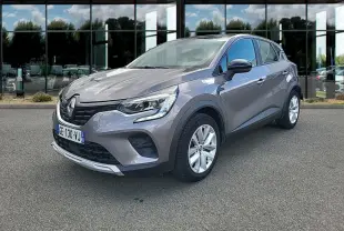 Renault Captur Business E-Tech hybride gris clair vu en 3/4 avant droit devant une vitrine réfléchissante.