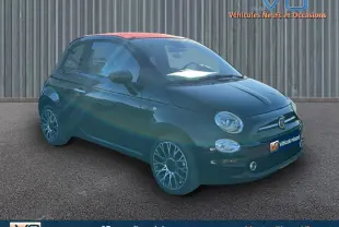 Fiat 500C noire vue 3/4 avant droit avec toit rouge et jantes alliage, stationnée devant un mur métallique.