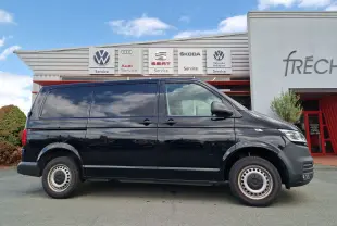 Profil côté droit d'un Volkswagen Transporter noir 2020 garé devant un centre de service multimarques.