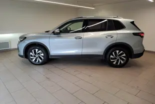 Volkswagen Tiguan 2025 argent Dolomite vu de profil côté gauche, jantes alliage et feux arrière allumés.