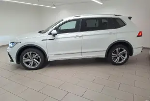 Vue de profil côté gauche du Volkswagen Tiguan Allspace blanc pur 2023 en finition R-Line avec jantes alliage et feux allumés.