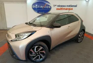 Toyota Aygo X beige vue 3/4 avant droit dans un showroom avec jantes noires et toit noir contrastant.