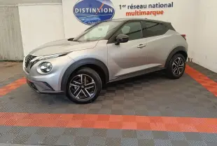 Vue de profil droit d'un Nissan Juke gris clair 2025 avec jantes alliage et toit noir dans un showroom.