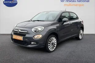 Fiat 500X gris foncé vue 3/4 avant droit, avec jantes alliage 18 pouces et phares antibrouillard allumés.