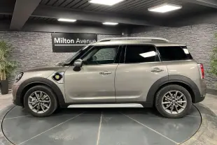 Profil droit d'une MINI Countryman Cooper SE gris métallisé avec jantes alliage 17 pouces et barres de toit longitudinales.