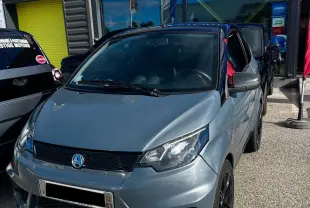 Vue 3/4 avant d'une AIXAM City Sport gris foncé avec jantes noires, stationnée devant un concessionnaire Ligier Store.
