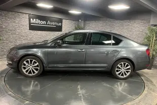 Profil côté gauche d'une Skoda Octavia gris métallisé 2020 en berline, avec jantes alliage 17 pouces, en intérieur showroom.
