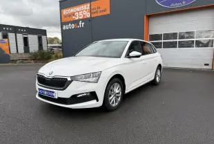 Vue 3/4 avant d'une Skoda Scala blanche stationnée devant un bâtiment commercial avec jantes alliage argent.