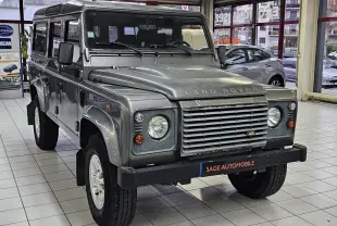 Vue 3/4 avant d'un Land Rover Defender 110 Station Wagon S gris, avec calandre distinctive et phare rond en intérieur showroom.