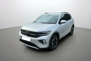 Volkswagen T-Cross gris argent en vue 3/4 avant droit, avec jantes alu 18 pouces et barres de toit noires.