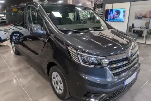 Renault Trafic Combi gris Comète vu en 3/4 avant droit dans un showroom lumineux avec détails chromés au niveau de la calandre.