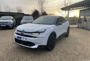 Citroën C4 hybride blanc Okenite avec toit noir Perla, vue 3/4 avant droit sur parking extérieur au coucher du soleil.