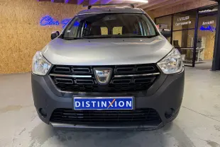 Vue frontale d'un Dacia Dokker gris avec calandre noire et logo au centre, stationné en intérieur showroom.