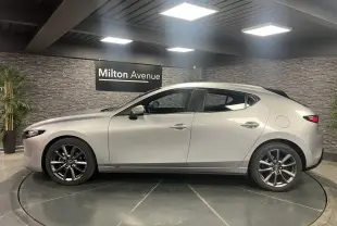 Profil côté gauche d'une Mazda3 gris métallisé 2023 avec jantes alliage 18 pouces dans un showroom.