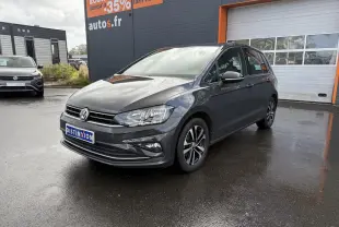 Volkswagen Golf Sportsvan gris Urano vue 3/4 avant droit sur parking devant un bâtiment commercial.