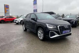 Audi Q2 noire vue en 3/4 avant droit sous la pluie, avec jantes alliage et calandre S line distinctive.