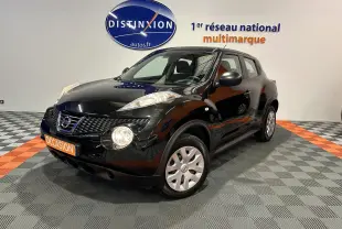 Nissan Juke noir métal en 3/4 avant droit, avec attelage visible, sur sol damier gris et orange en intérieur showroom.