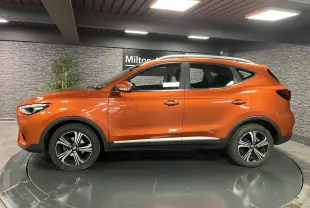 Profil côté gauche du SUV MG ZS 2022 orange métallisé avec jantes alliage et barres de toit visibles.