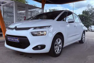 Citroën C4 Picasso blanc vue 3/4 avant droit, avec calandre noire et phares allumés sous un abri orange.