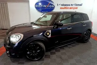 Vue 3/4 avant droit d'une MINI Countryman Cooper SE bleu foncé avec jantes noires et toit noir dans un showroom.