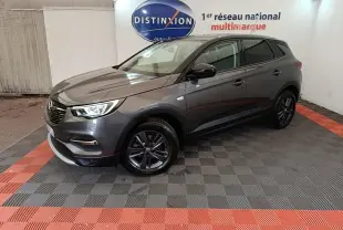 Opel Grandland X gris foncé en 3/4 avant droit, avec jantes noires et phares LED allumés, en intérieur showroom.