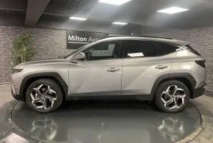 Vue de profil côté gauche du Hyundai Tucson gris métallisé 2023 avec jantes alliage et toit noir contrasté.