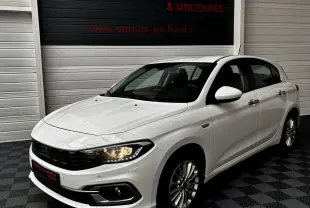 Vue 3/4 avant droite d'une Fiat Tipo blanche 2021 avec phares allumés dans un garage.