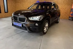BMW X1 noir vue 3/4 avant droit dans un showroom avec calandre et phares allumés visibles.