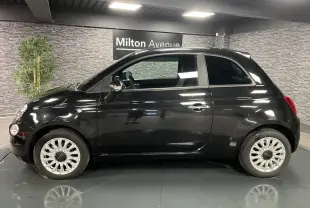 Profil côté gauche d'une Fiat 500 noire 2023 avec jantes alliage et poignées chromées dans un showroom.