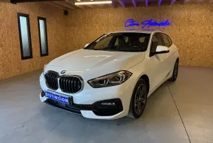 BMW Série 1 118i blanc en 3/4 avant droit, avec calandre chromée et jantes bi-ton dans un showroom.