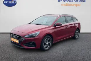 Vue 3/4 avant droite d'une Hyundai i30 SW 2023 Sunset Red Metal avec jantes alliage et calandre distinctive.