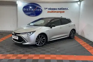 Toyota Corolla Hybride gris clair vue 3/4 avant droit, avec jantes alliage et phares LED allumés.