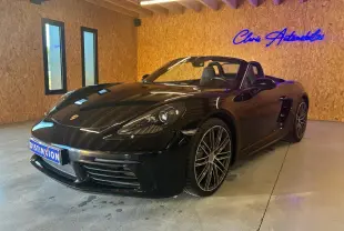Porsche 718 Boxster 2.0 300 noir vue 3/4 avant droit en intérieur avec jantes alliage et capote ouverte.