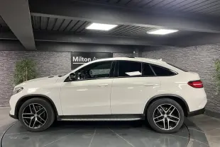 Profil côté gauche du Mercedes GLE Coupé 350 d blanc avec jantes AMG noires et toit panoramique en intérieur showroom.