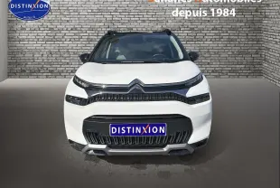 Vue frontale d'un Citroën C3 Aircross blanc avec toit noir et détails noirs brillants sur un fond de mur en briques.
