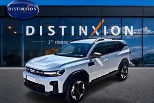 Dacia Bigster blanc en 3/4 avant droit, avec barres de toit et jantes alu distinctives, devant showroom Distinxion.