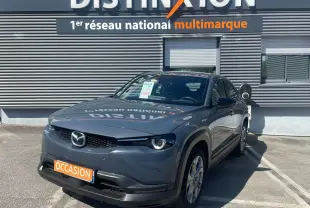 Mazda MX-30 électrique gris Polymetal en 3/4 avant droit, stationnée devant un mur gris avec panneau Distinxion.