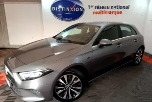 Vue 3/4 avant droit d'une Mercedes Classe A 250 e Business Line gris foncé avec phares LED allumés en intérieur showroom