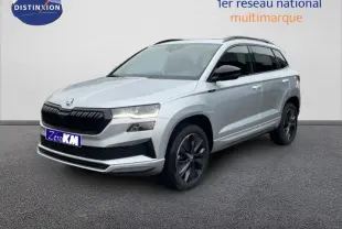 Vue 3/4 avant d'un Skoda Karoq argent 2025 avec barres de toit et jantes noires sur fond neutre.