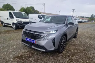 Peugeot 3008 gris Artense vue 3/4 avant droit, avec calandre distinctive et phares LED allumés sur terrain gravillonné.