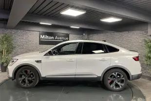 Profil côté gauche d'un Renault Arkana blanc perle 2022 R.S. Line avec jantes noires et accents rouges en intérieur showroom.