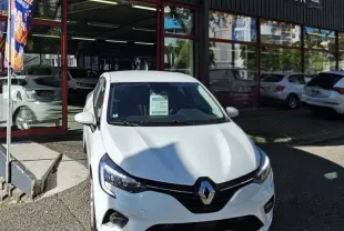 Renault Clio blanc glacier vue de face, stationnée devant un garage avec enseigne AD Expert.
