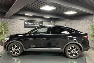 Profil côté gauche du Renault Arkana noir métal 2021 avec jantes alliage 18 pouces dans un showroom intérieur.
